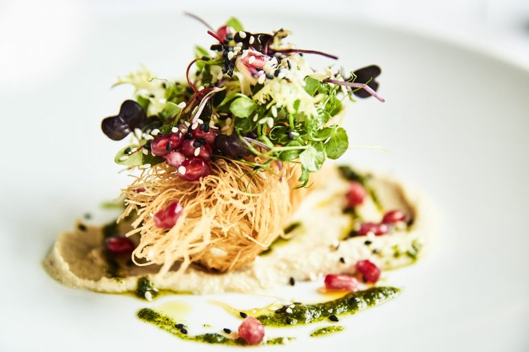 Ein Gourmet-Gericht im Restaurant Rolin mit einer knusprigen Vorspeise aus regionalen Produkten und frischen Kräutern, belegt mit Granatapfelkernen, serviert auf einer cremigen Sauce mit Kräuteröltupfern.