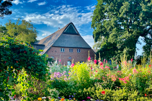 Old farmhouse in the Ellerhoop Arboretum surrounded by trees and a profusion of flowers in the foreground.